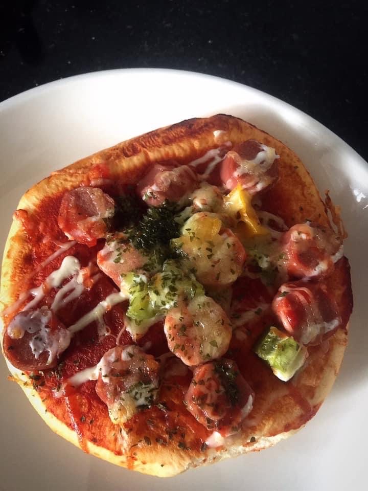 A close-up of a delicious mini pizza or savory bread topped with sausage, cheese, and herbs.