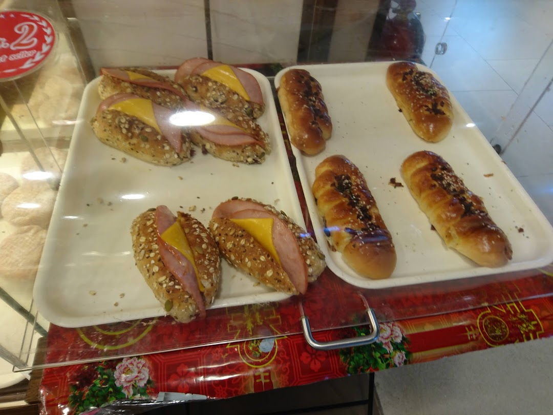 A display case showcasing freshly baked savory ham and cheese buns alongside sweet sesame and chocolate bread.