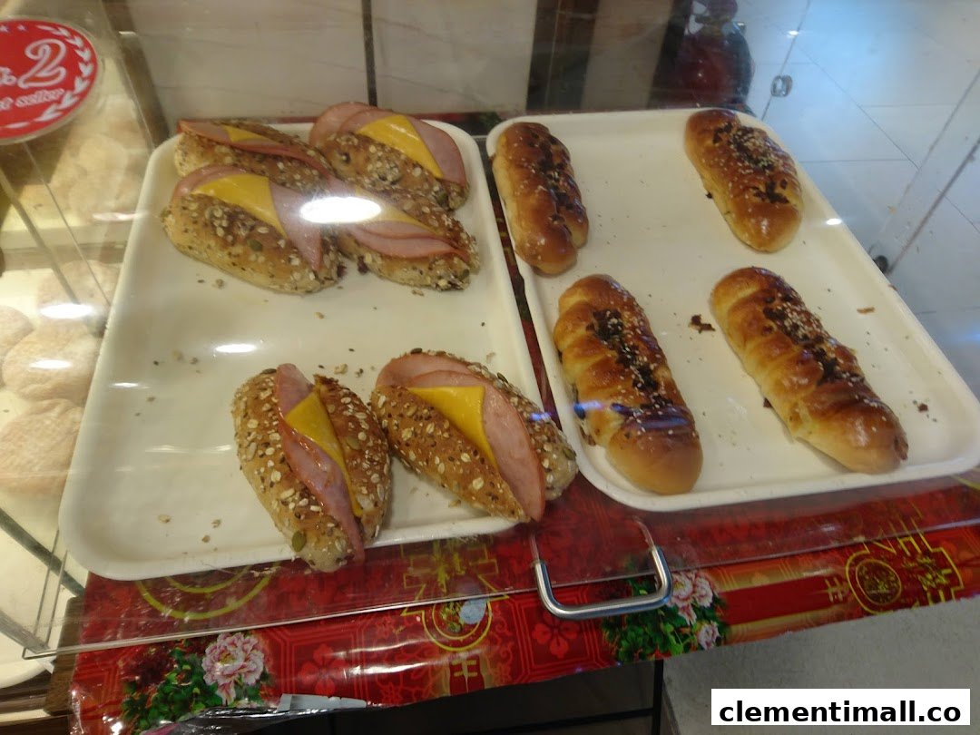 A display case showcasing freshly baked savory ham and cheese buns alongside sweet sesame and chocolate bread.