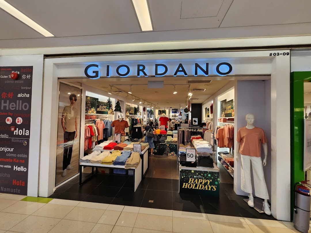 The brightly lit entrance of a Giordano clothing store, featuring mannequins, displays, and holiday decorations.