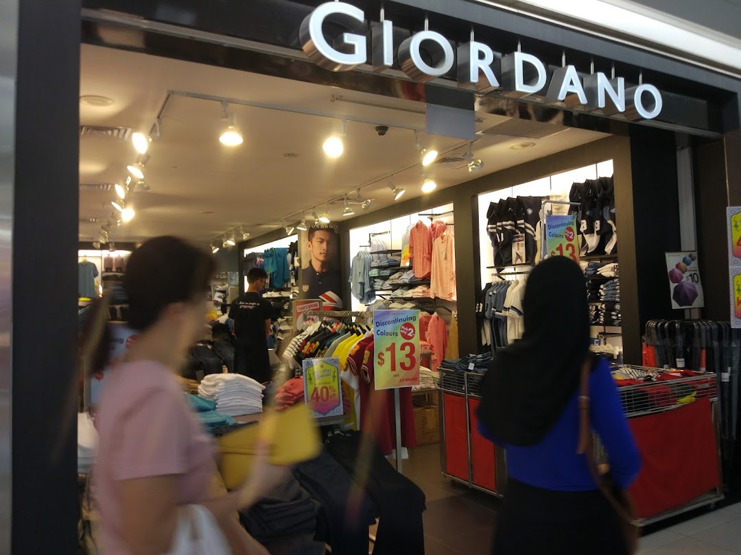 The entrance of a Giordano clothing store, showcasing apparel displays and customers inside.