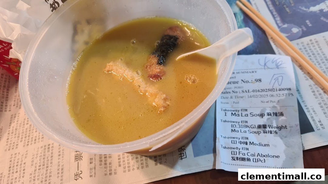 A close-up of a takeaway bowl of Ma La Soup with ingredients, a spoon, chopsticks, and a receipt.