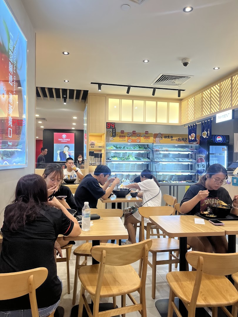 Customers enjoy customizable mala tang in a brightly lit, modern eatery with a fresh ingredient display.