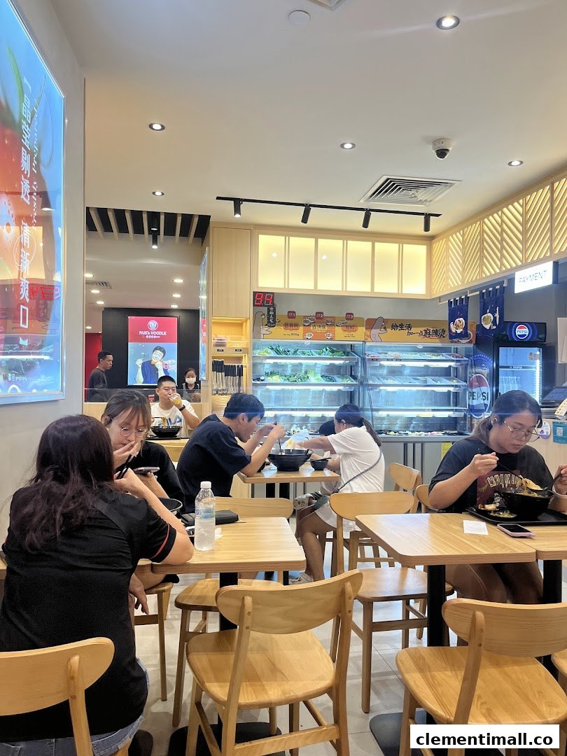 Customers enjoy customizable mala tang in a brightly lit, modern eatery with a fresh ingredient display.