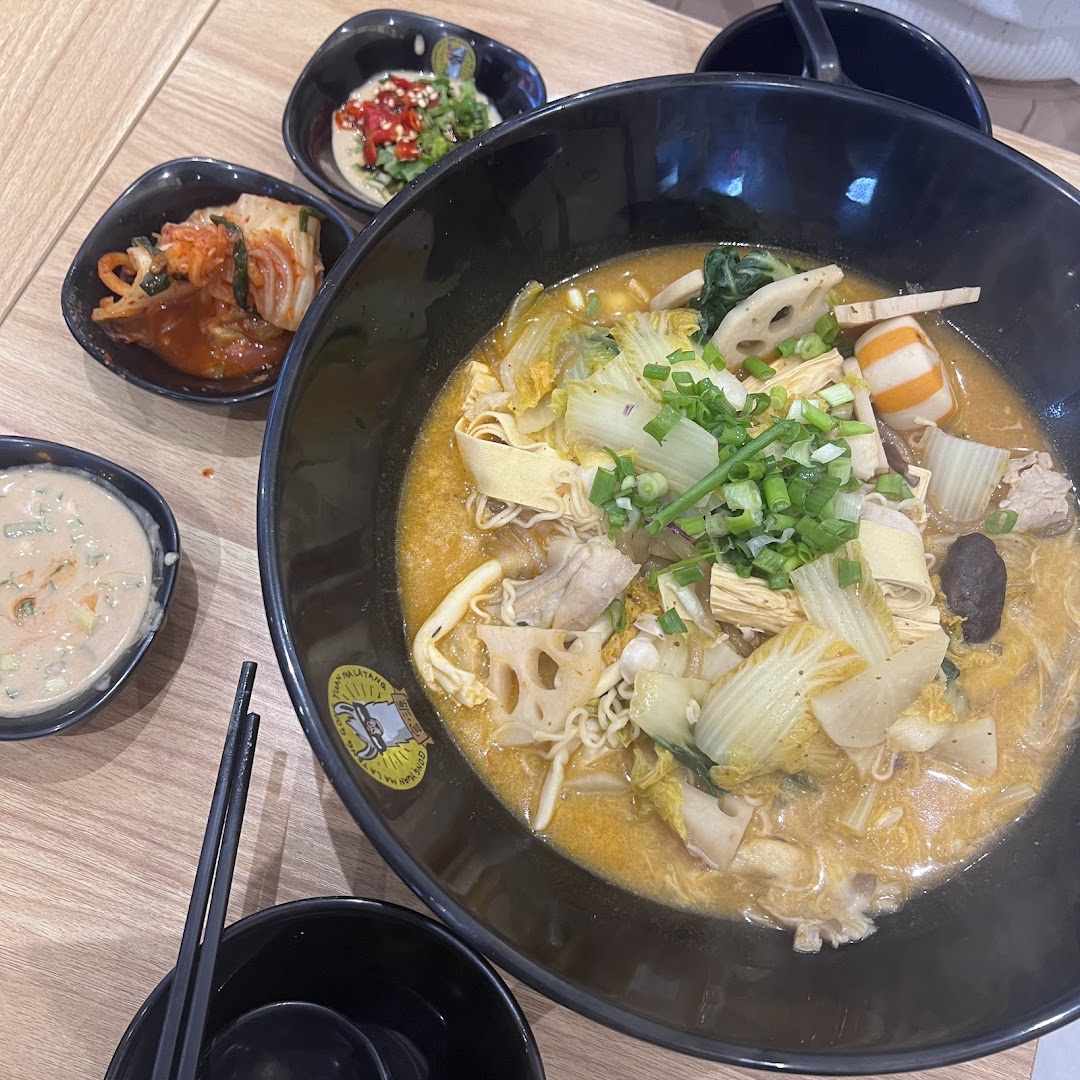 A vibrant bowl of Mala Tang with assorted ingredients and accompanying side dishes on a wooden table.
