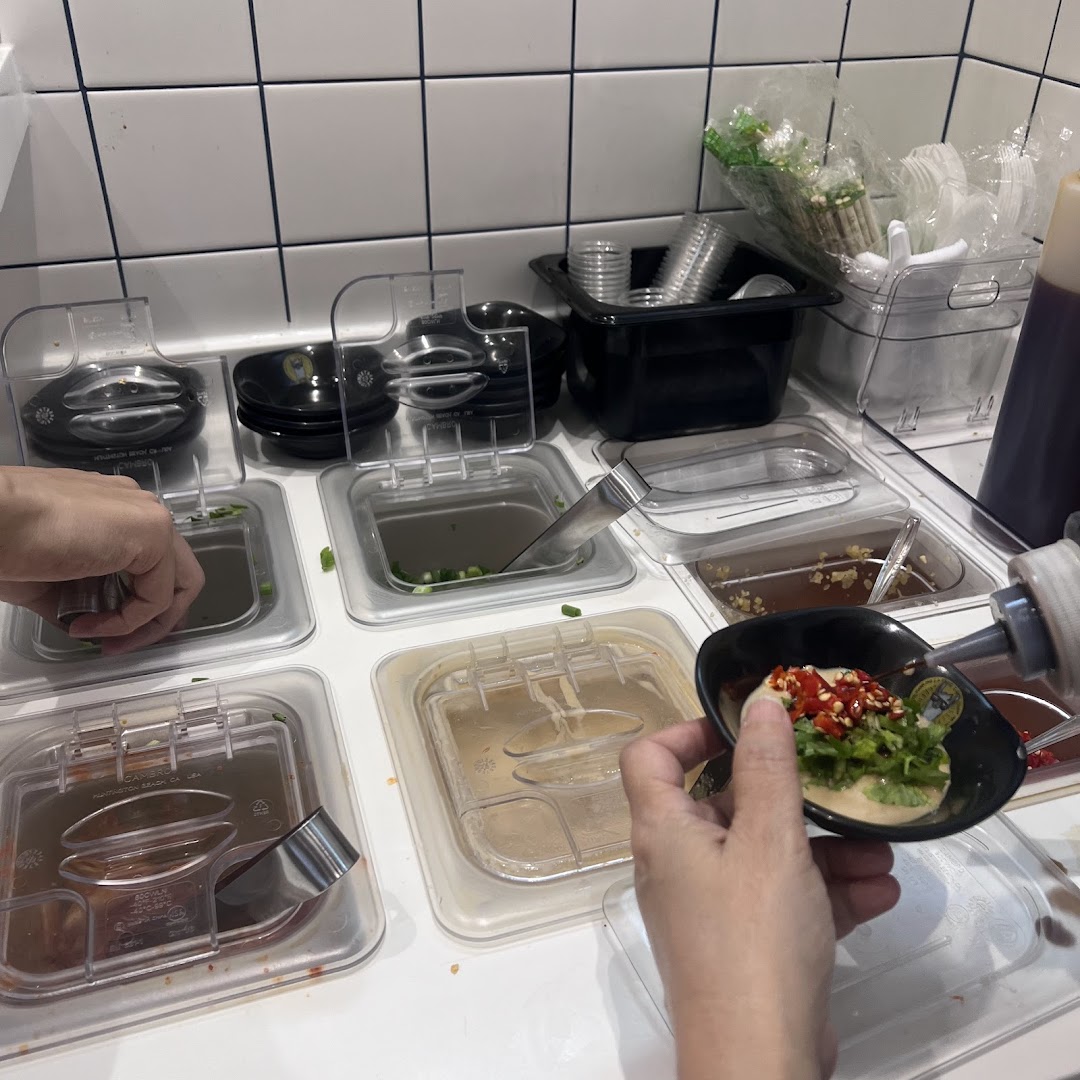 A customer customizes their sauce at a self-service condiment station with various toppings.