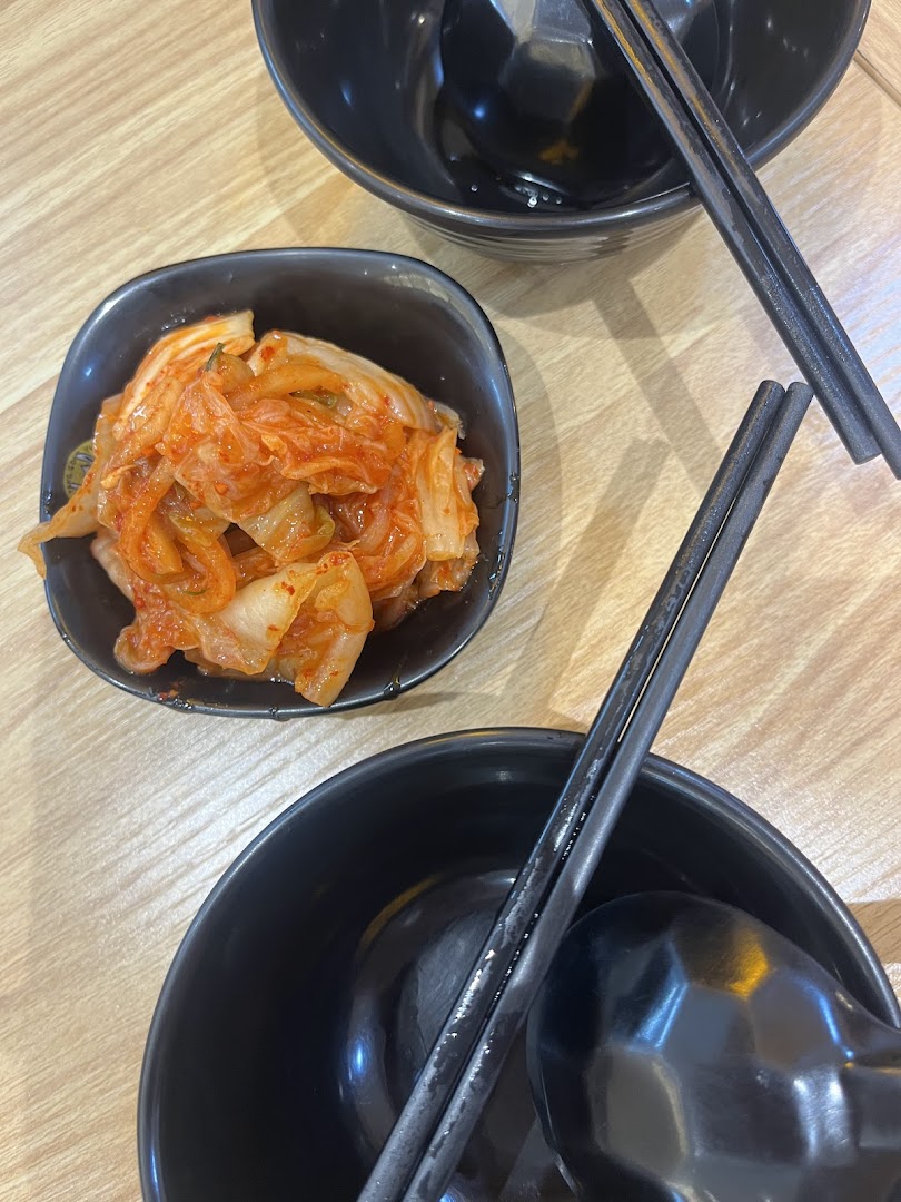 A small bowl of kimchi and two empty black bowls with chopsticks on a wooden table.