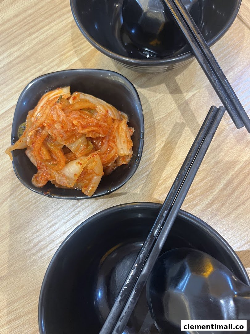 A small bowl of kimchi and two empty black bowls with chopsticks on a wooden table.