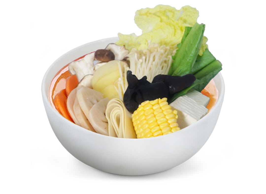 A vibrant bowl of Mala Tang ingredients including vegetables, mushrooms, and corn in a white bowl.