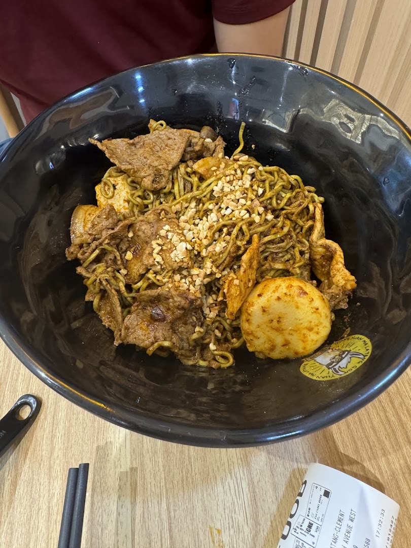 A close-up of a large bowl of green noodles with beef slices and crushed peanuts.