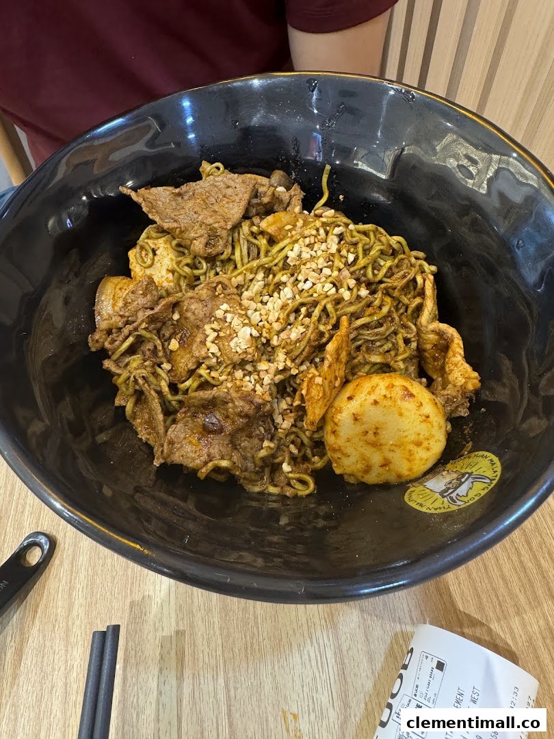 A close-up of a large bowl of green noodles with beef slices and crushed peanuts.