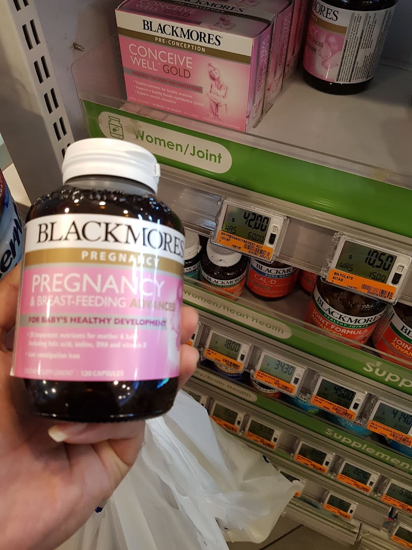 A hand holds a Blackmores pregnancy supplement bottle in a health and beauty store aisle.