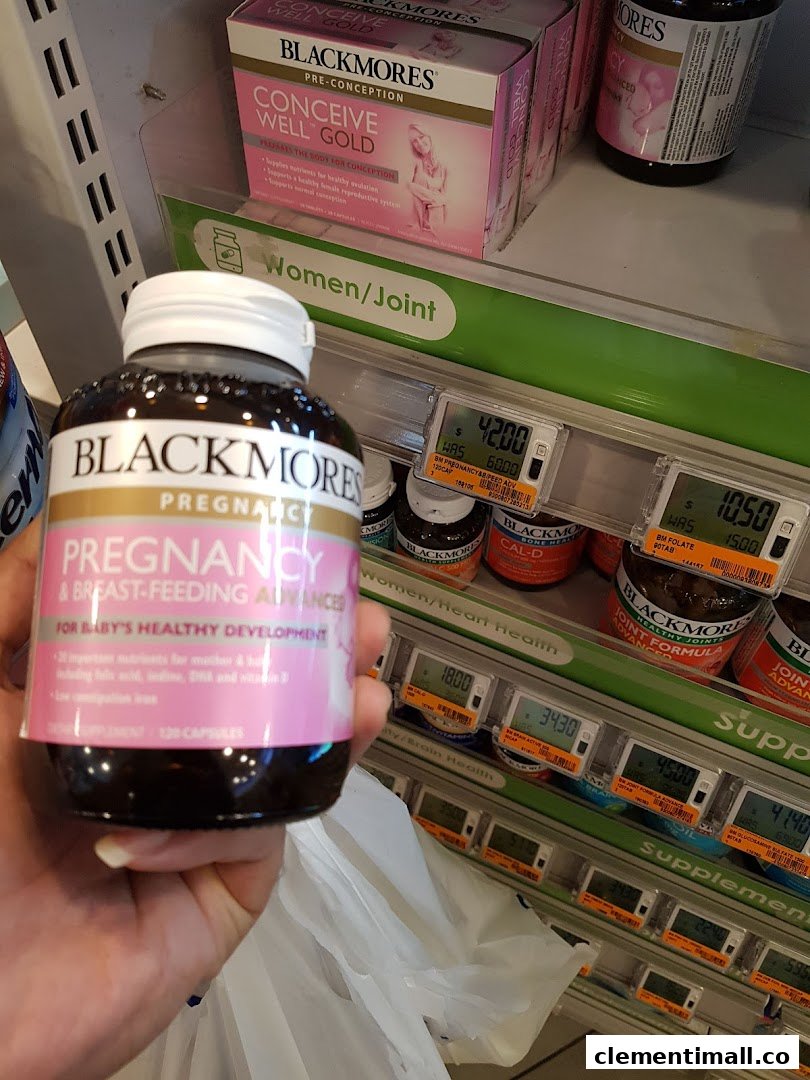 A hand holds a Blackmores pregnancy supplement bottle in a health and beauty store aisle.