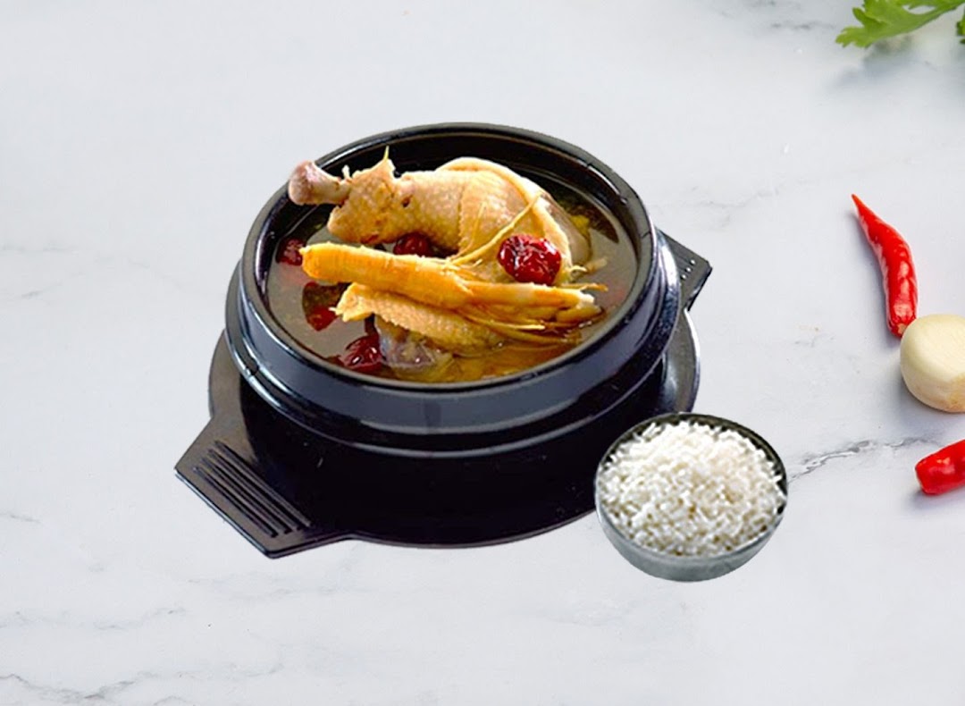 A traditional Korean chicken soup (Samgyetang) served in a black pot with a side of rice.