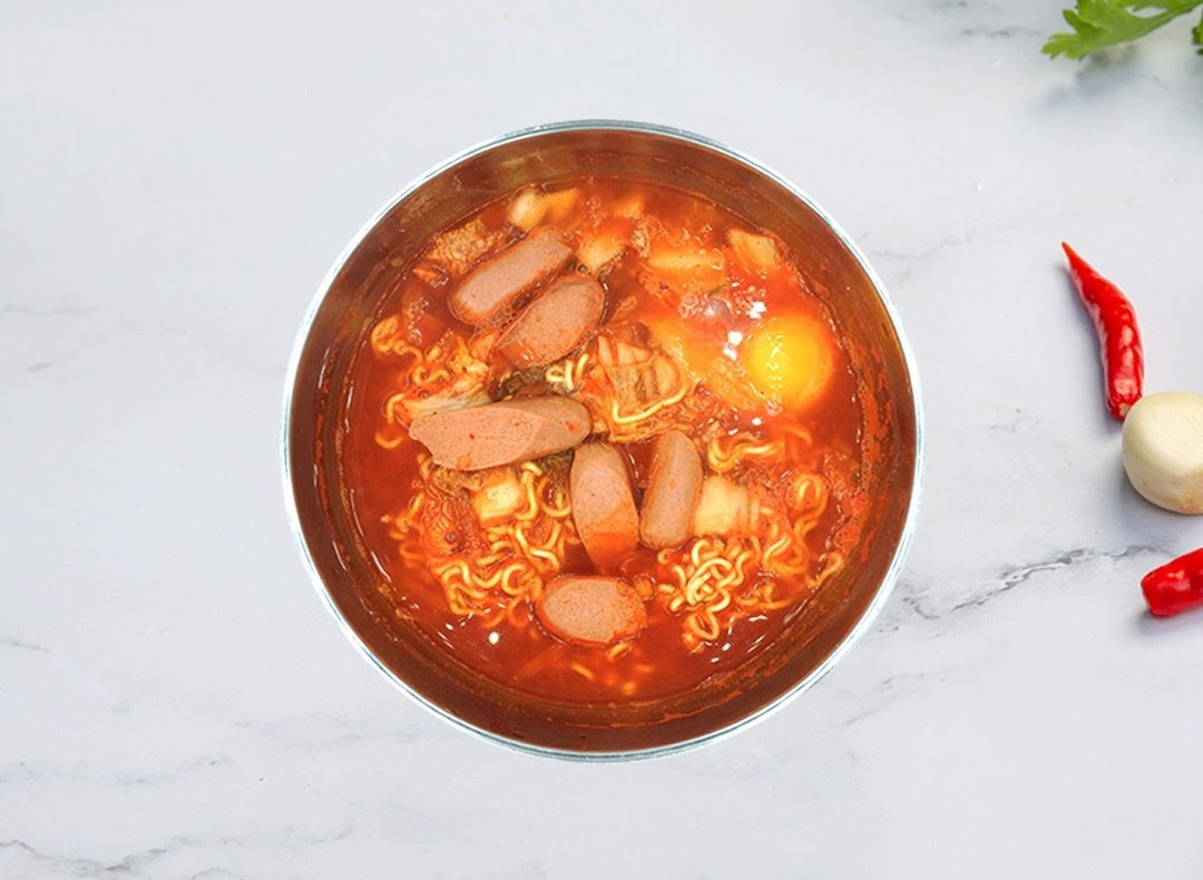 A vibrant bowl of Korean ramen with sausage, kimchi, and a raw egg yolk.