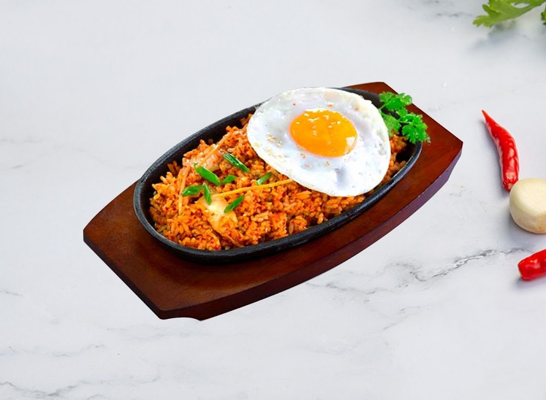 A sizzling plate of Korean fried rice topped with a perfectly cooked fried egg and fresh garnishes.