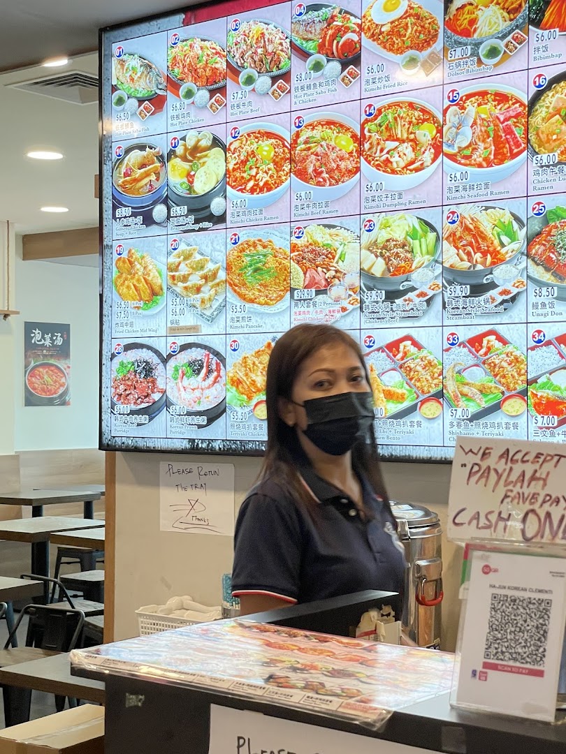 A large digital menu board displaying various Korean dishes with prices, alongside a staff member at the counter.