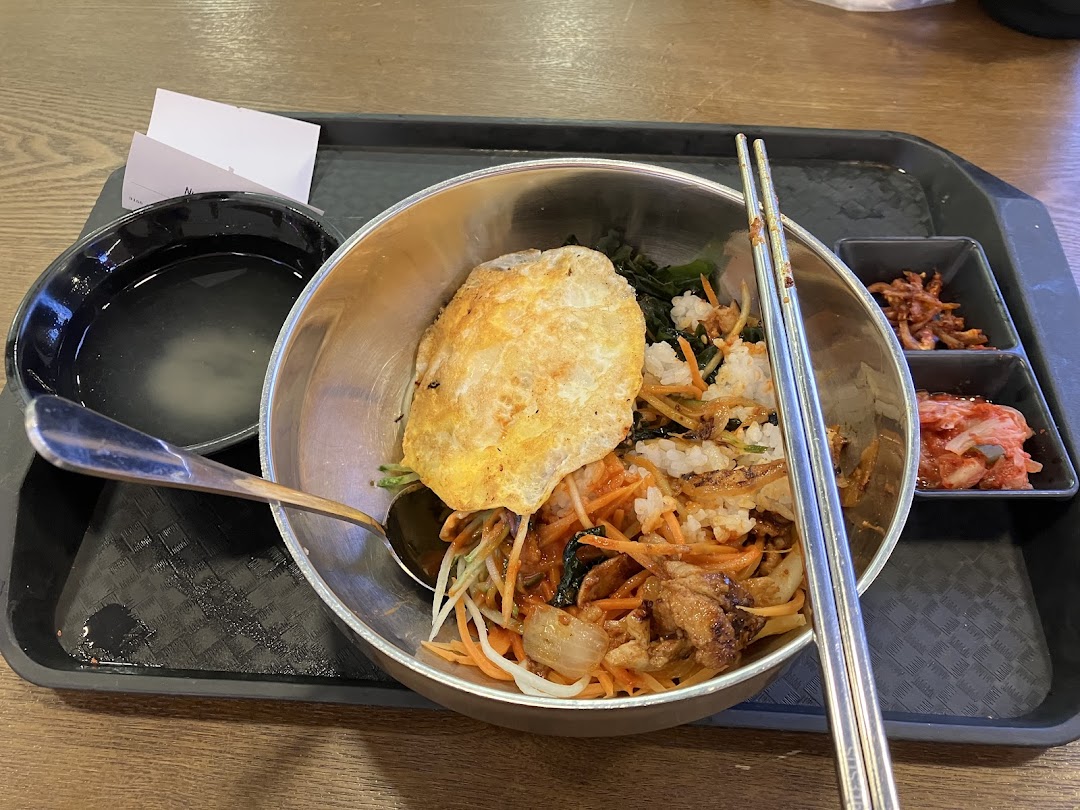 A vibrant bowl of Korean bibimbap with side dishes and soup on a tray.