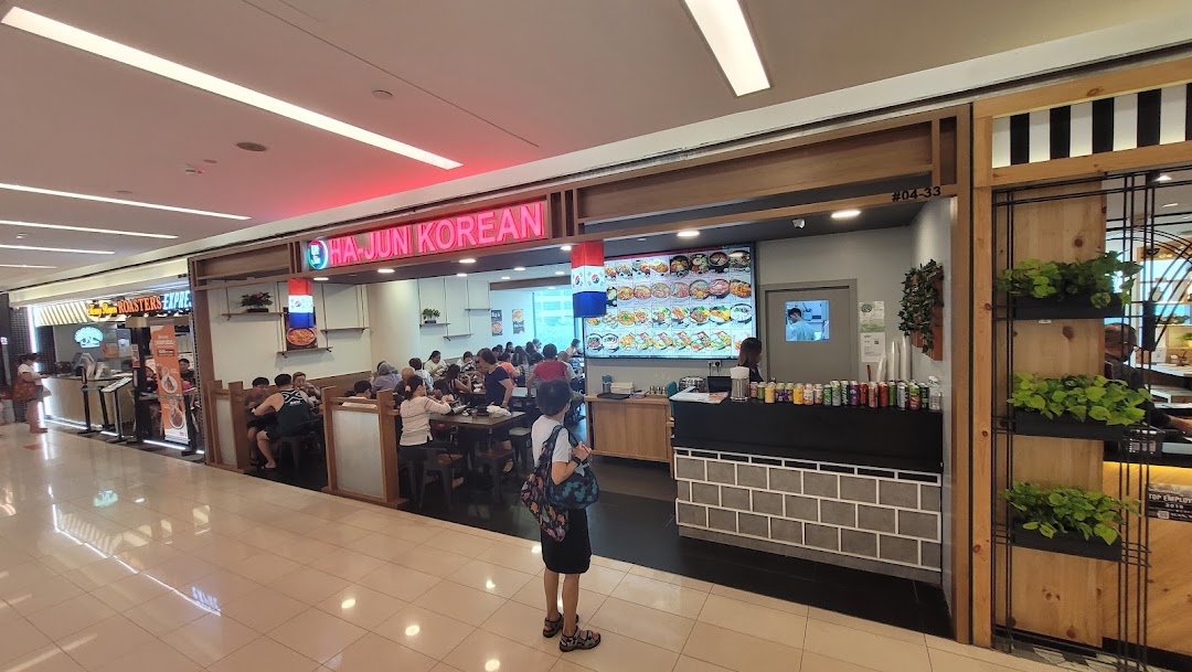 Ha-Jun Korean restaurant's bustling entrance, showcasing diners and a vibrant digital menu board.
