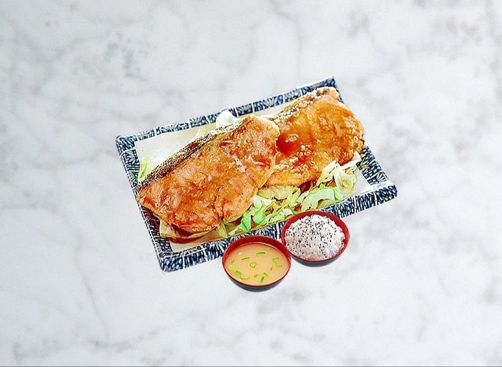 A delicious Korean-style fried fish dish served with rice and miso soup on a marble surface.