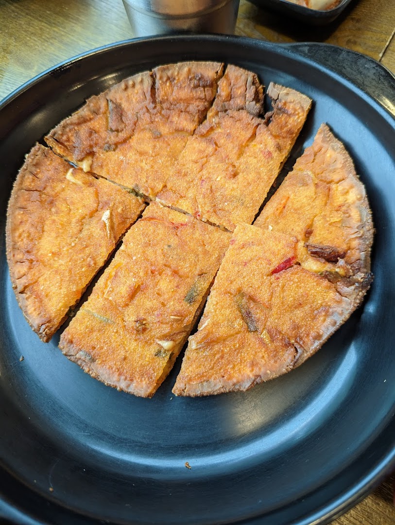 A golden-brown Korean pancake (Jeon) cut into slices, served on a black plate.