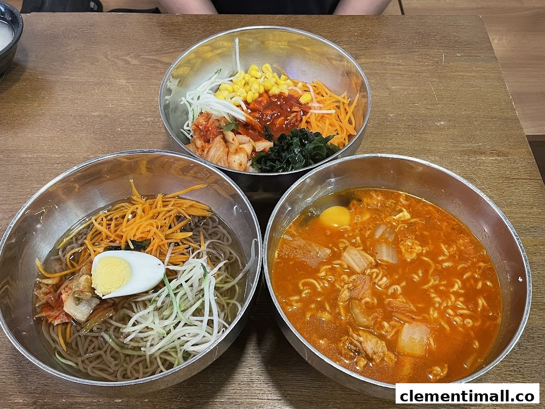 Three vibrant bowls of Korean dishes, including cold noodles, spicy ramen, and bibimbap, served on a wooden table.