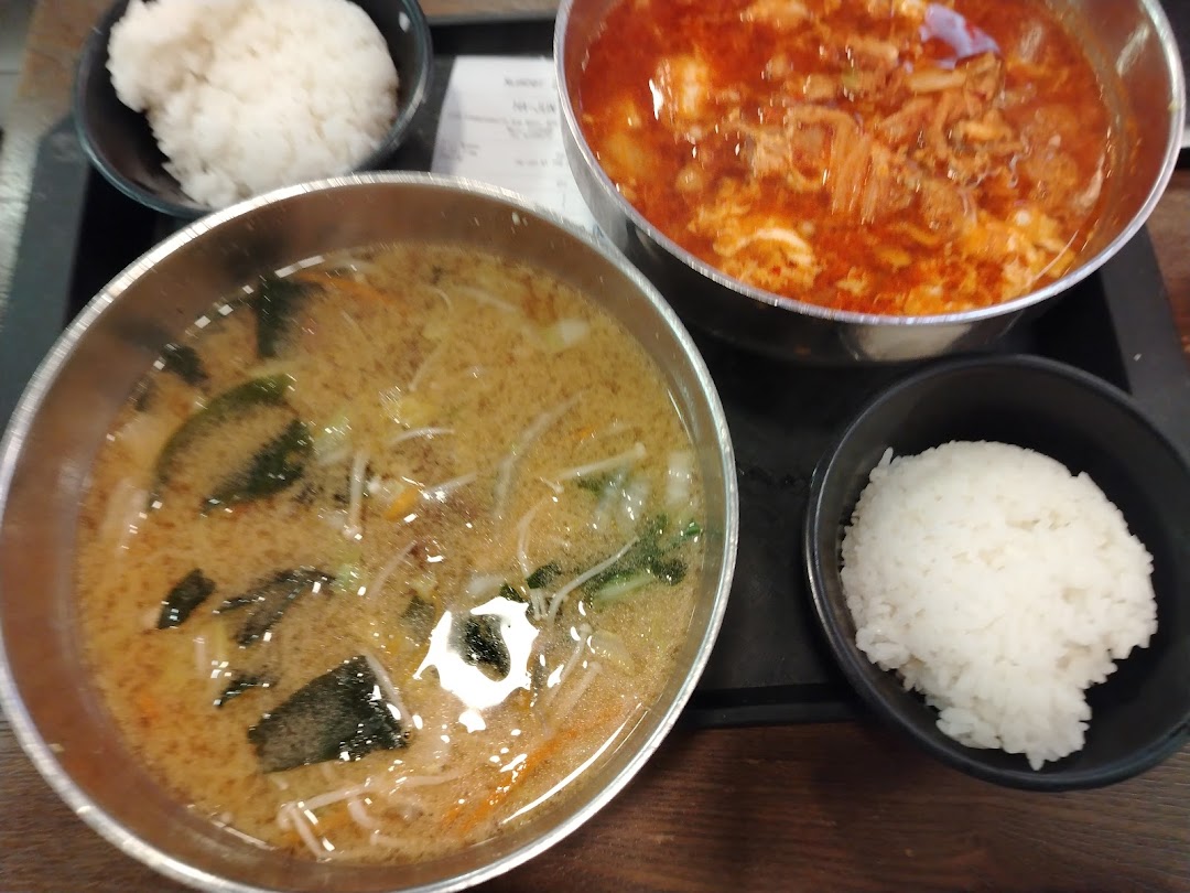 Two bowls of Korean soup or stew with accompanying bowls of white rice.