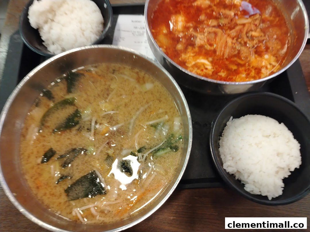 Two bowls of Korean soup or stew with accompanying bowls of white rice.