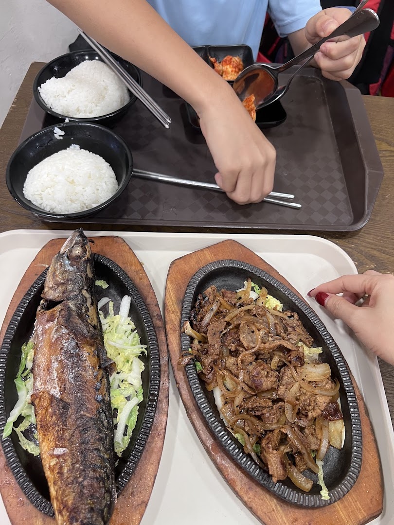 Diners enjoying sizzling Korean dishes, including grilled fish and bulgogi, with rice and kimchi.