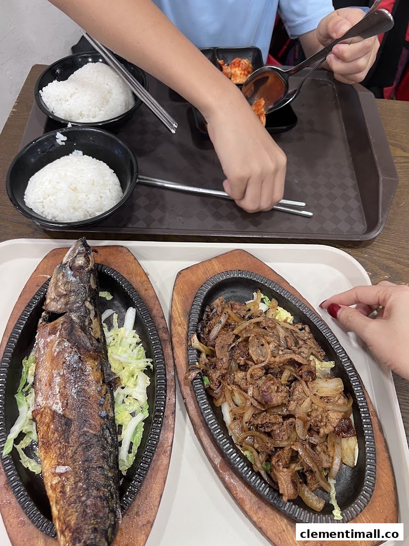Diners enjoying sizzling Korean dishes, including grilled fish and bulgogi, with rice and kimchi.