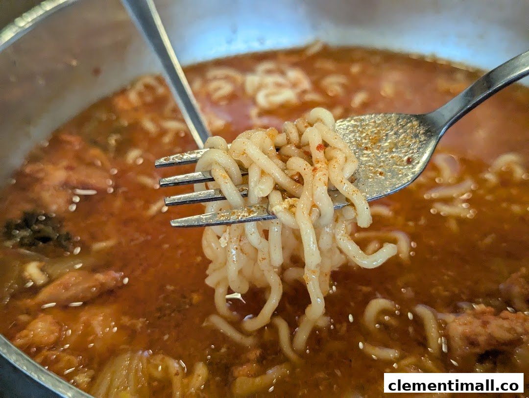 A close-up of a fork lifting spicy noodles from a steaming bowl of Korean ramen.