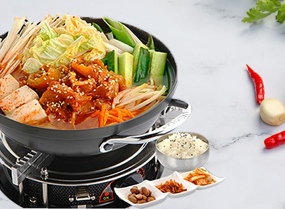 A vibrant Korean hot pot with various ingredients, served with rice and traditional side dishes.