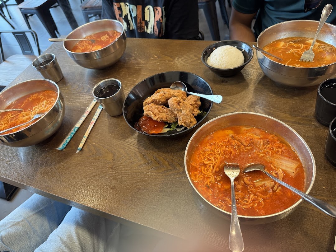 A table laden with several bowls of spicy Korean ramen, fried chicken, and rice at Ha-Jun Korean.