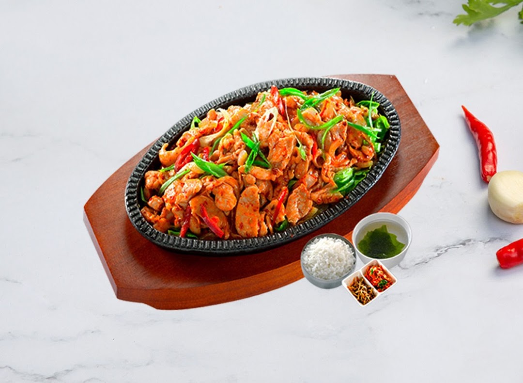 A sizzling Korean stir-fry dish with chicken, vegetables, rice, and side dishes on a hot plate.