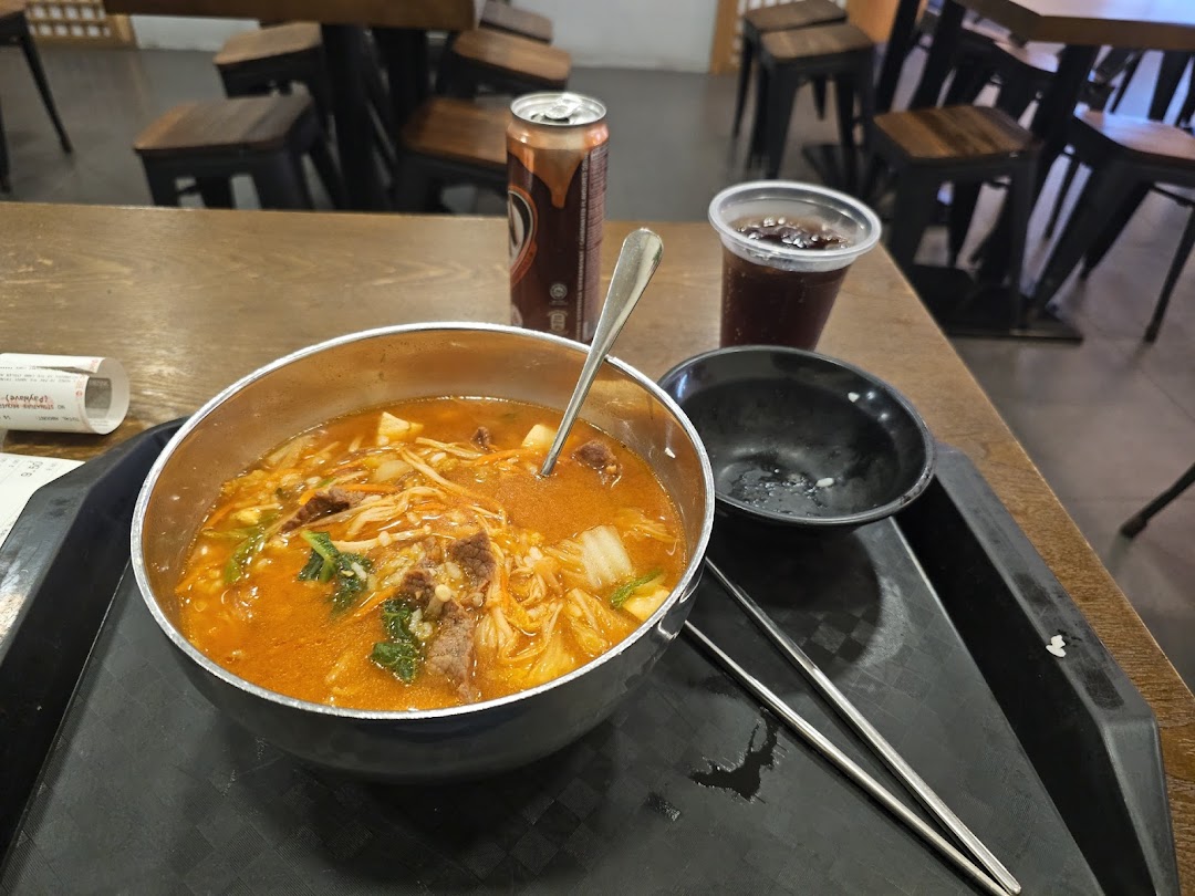 A vibrant bowl of Korean stew with beef and vegetables, served with drinks and chopsticks on a table.