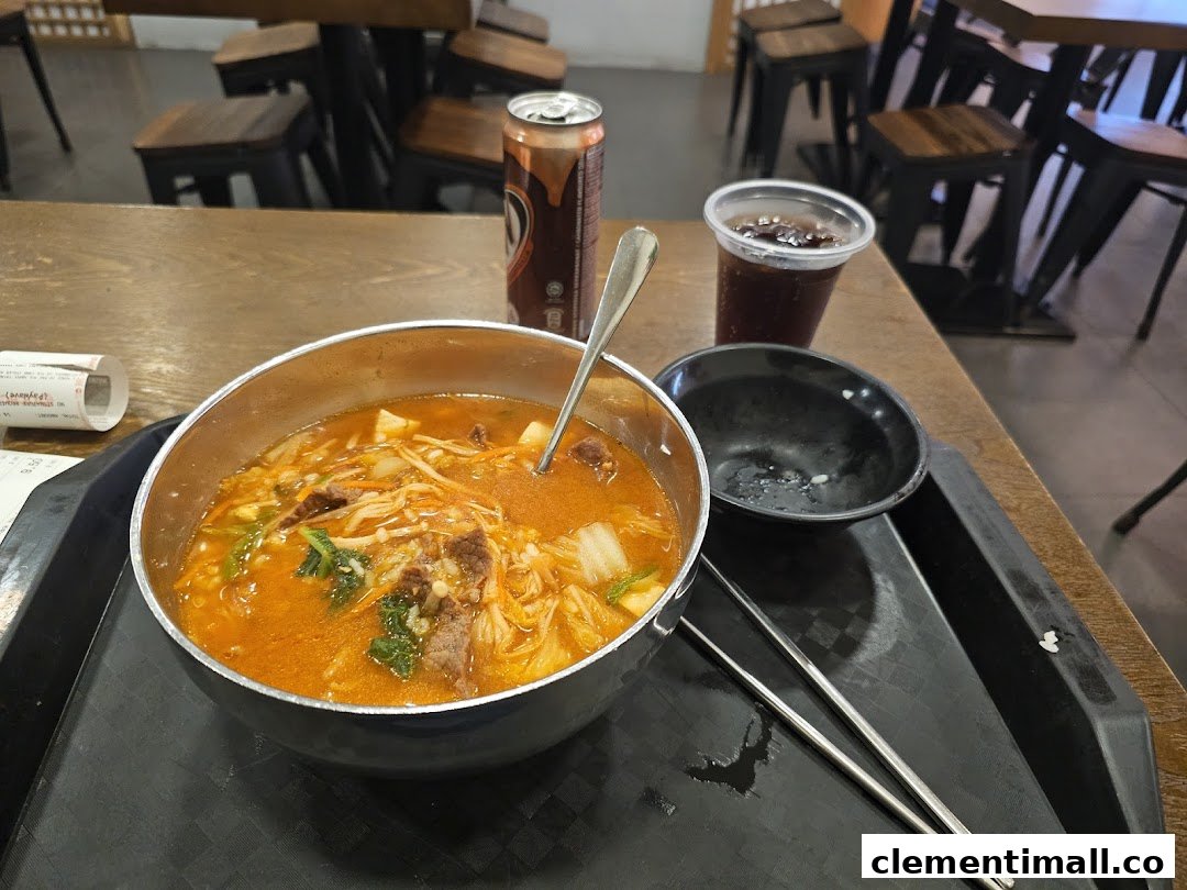 A vibrant bowl of Korean stew with beef and vegetables, served with drinks and chopsticks on a table.