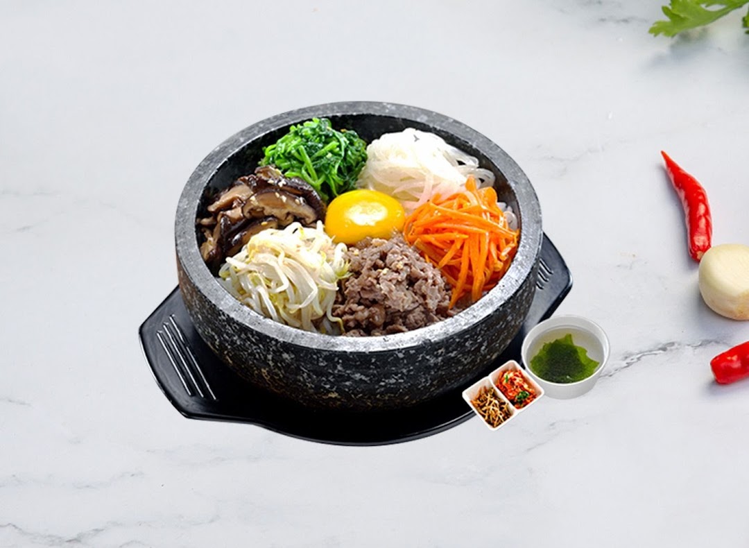 A vibrant Korean bibimbap dish served in a hot stone bowl with various toppings and side dishes.