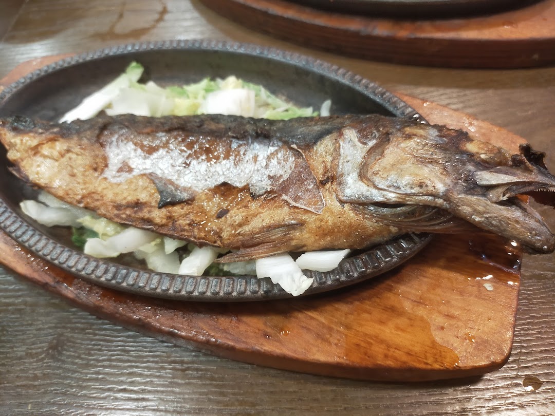 A whole grilled fish served on a sizzling plate with fresh vegetables at Ha-Jun Korean.