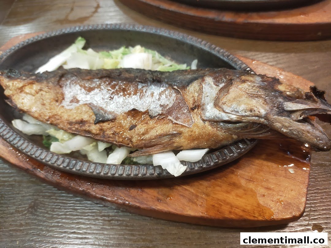 A whole grilled fish served on a sizzling plate with fresh vegetables at Ha-Jun Korean.
