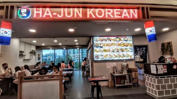 The interior of Ha-Jun Korean restaurant, featuring a vibrant menu display and diners enjoying their meals.