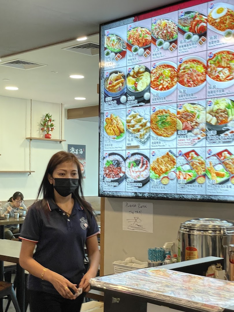 A digital menu board at Ha-Jun Korean showcasing various dishes with prices, alongside a staff member.