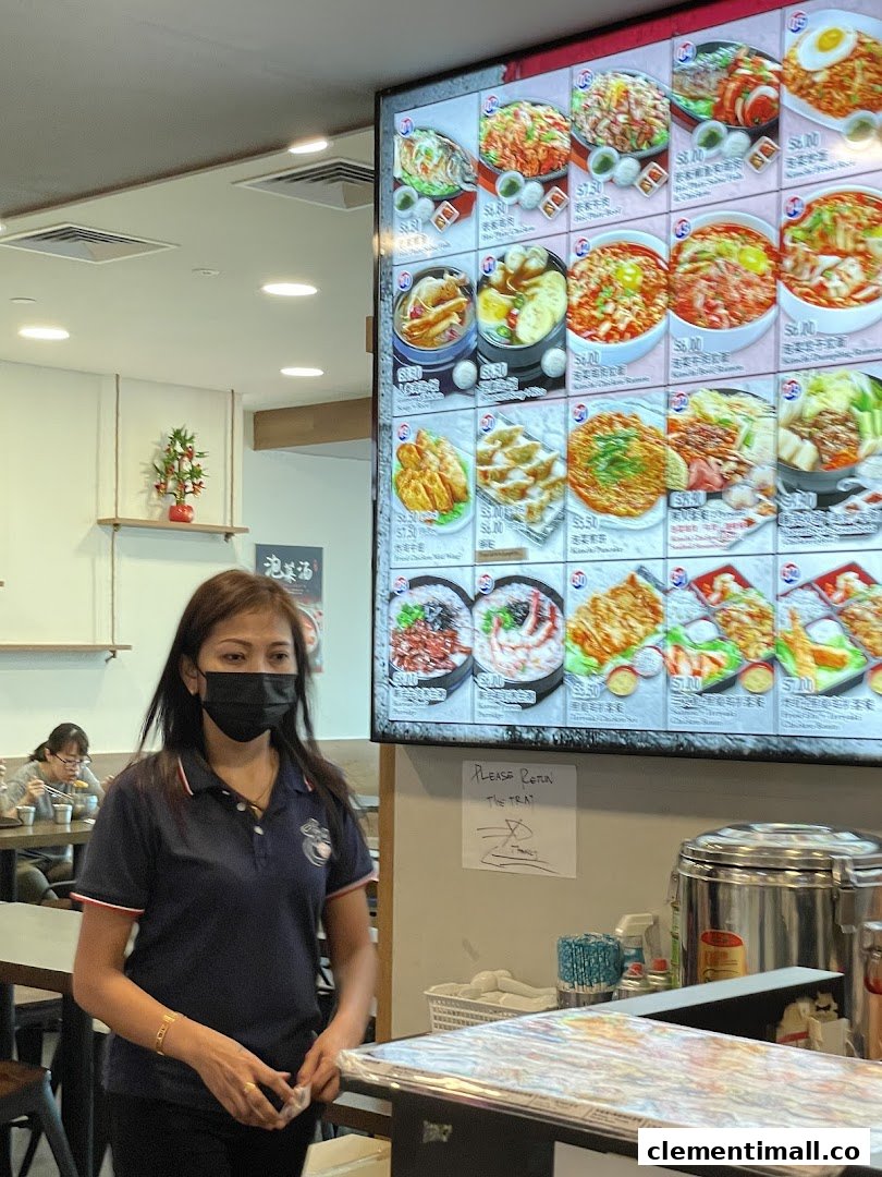 A digital menu board at Ha-Jun Korean showcasing various dishes with prices, alongside a staff member.