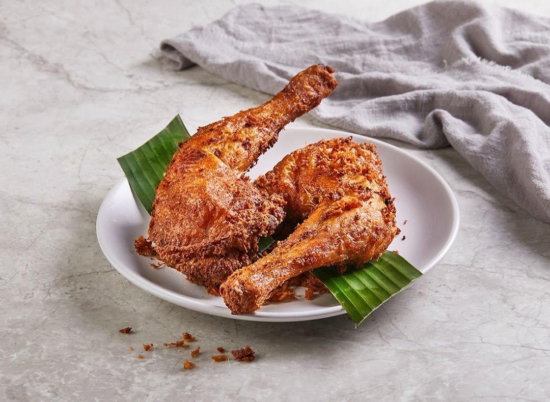 Two crispy fried chicken pieces, garnished with banana leaves, served on a white plate.
