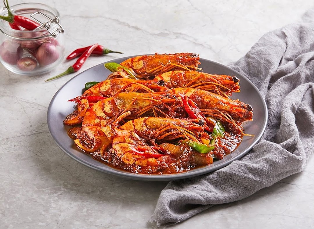 A plate of large, spicy prawns in a rich red sauce, garnished with chili and bell peppers.