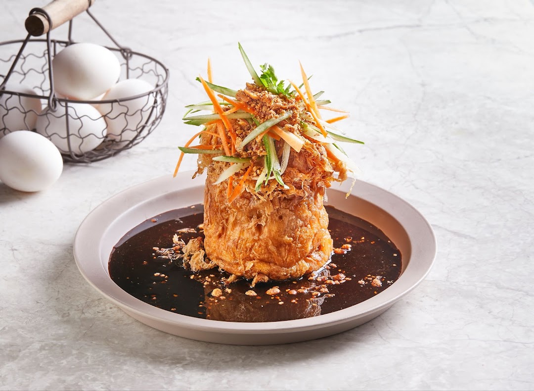 A beautifully presented fried egg dish with rich sauce and fresh julienned vegetables, alongside a basket of eggs.