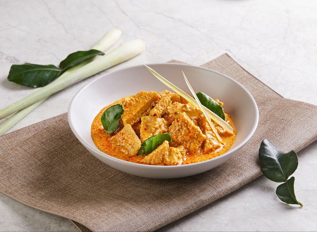 A vibrant bowl of traditional Malay curry with tender pieces and aromatic herbs like lemongrass and kaffir lime.