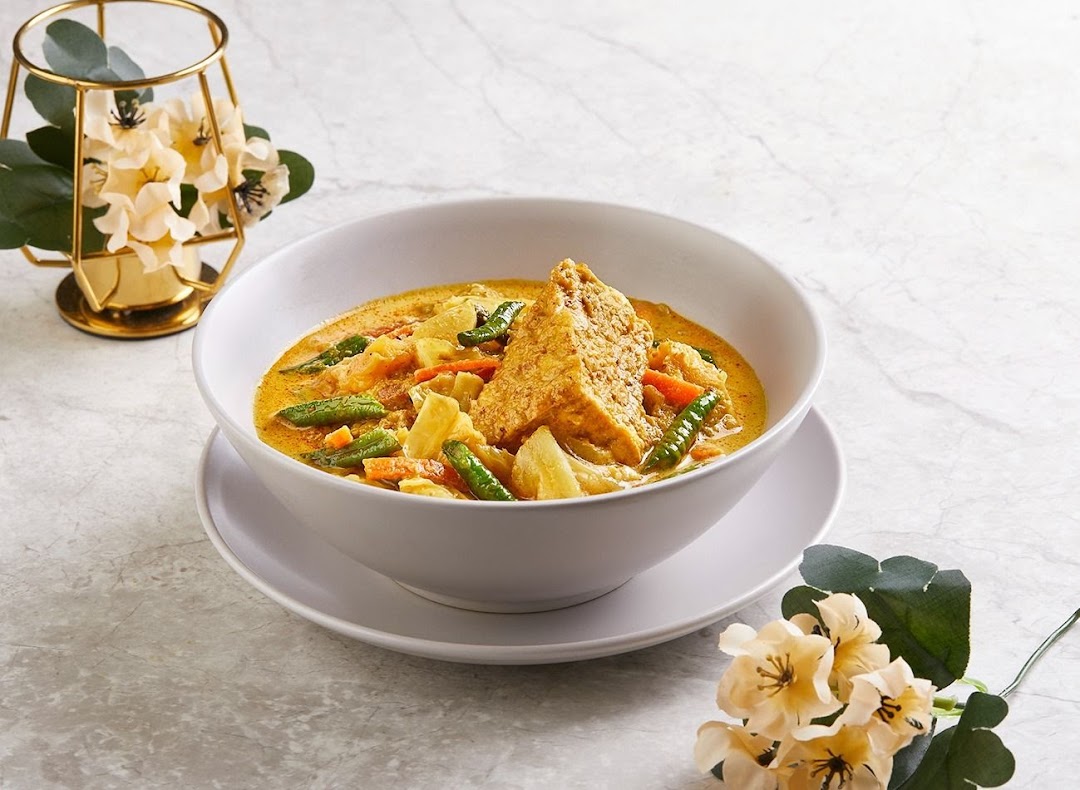 A vibrant bowl of yellow curry or stew with vegetables and a large piece of fried tofu.