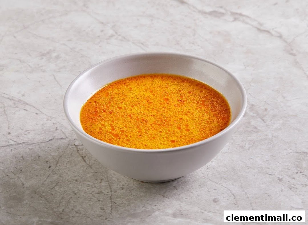 A white bowl filled with vibrant orange soup, possibly curry or broth, on a grey marbled surface.