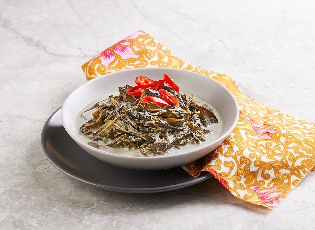 A bowl of traditional Indonesian or Malay dish featuring leafy greens in a creamy coconut sauce, garnished with red chilies.