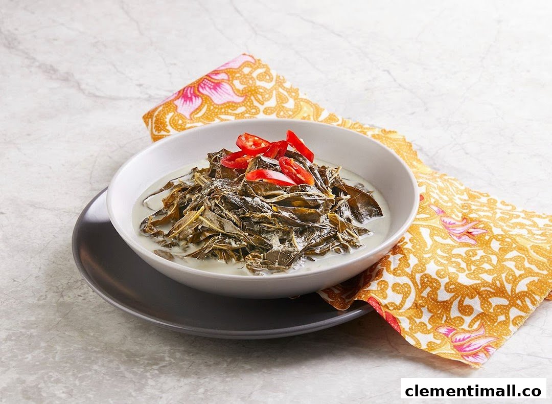 A bowl of traditional Indonesian or Malay dish featuring leafy greens in a creamy coconut sauce, garnished with red chilies.